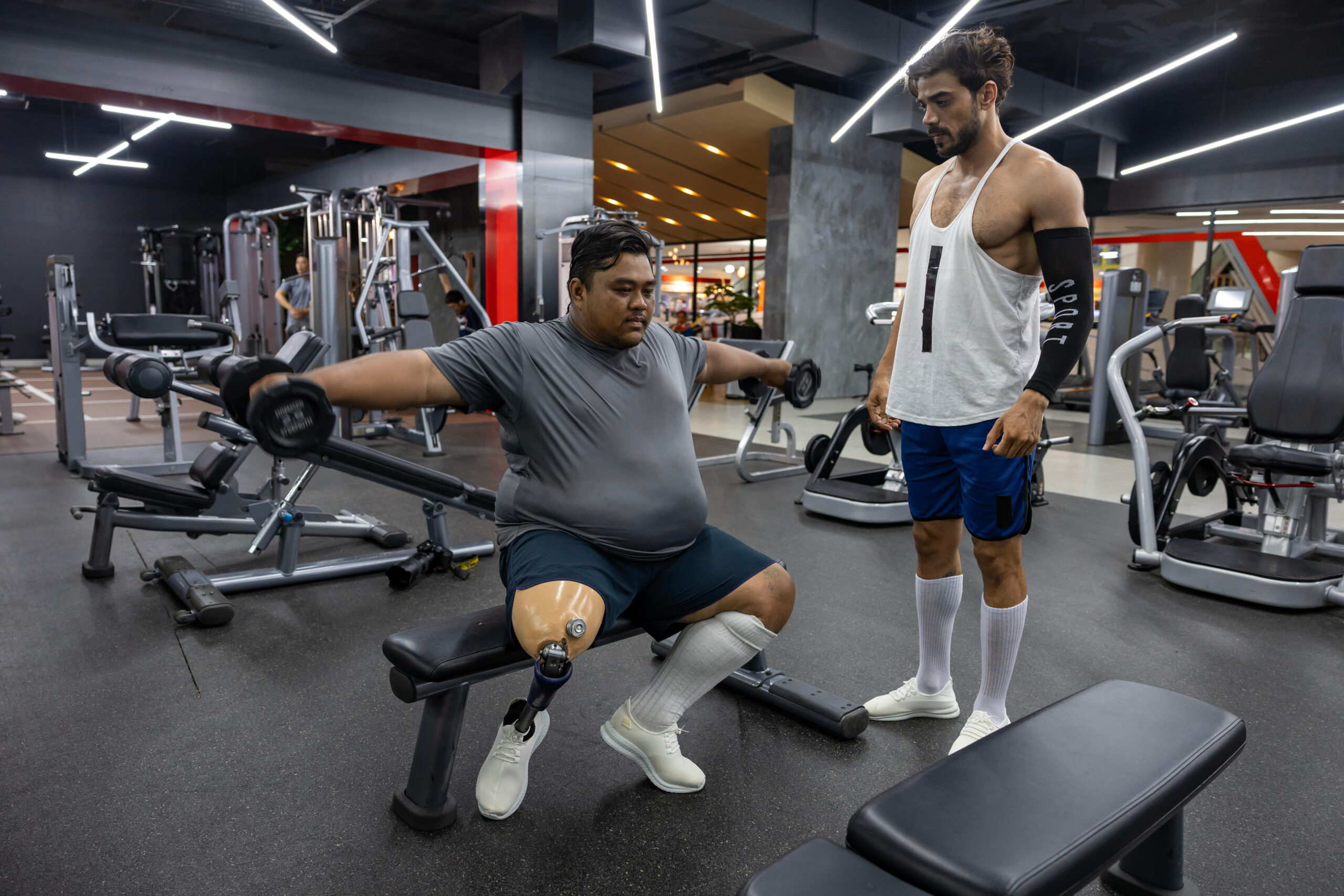 Fitness Coaching Motivation Physical Training A personal trainer guiding a client with a prosthetic leg through a workout, showcasing the dedication and support required for fitness success. This image highlights the power of personalized coaching in overcoming physical challenges, a core principle of the Muscle Mastery method. Image by Jeff Later – founder of L8R Lifestyle.